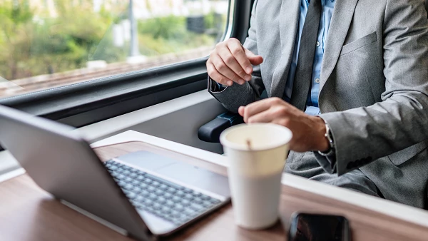 Geschäftsmann im Zug mit Laptop und Kaffeebecher
