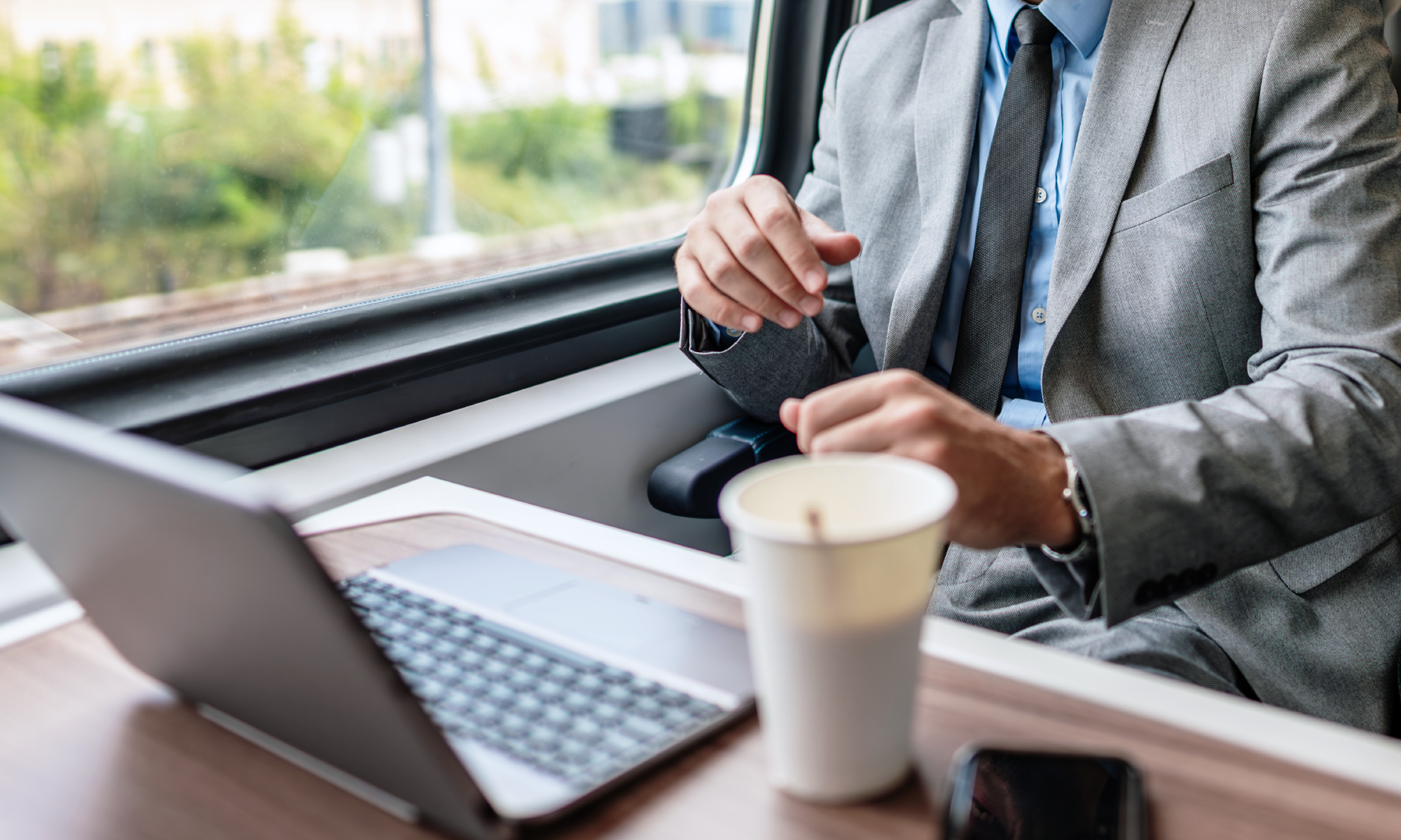 Geschäftsmann im Zug mit Laptop und Kaffeebecher