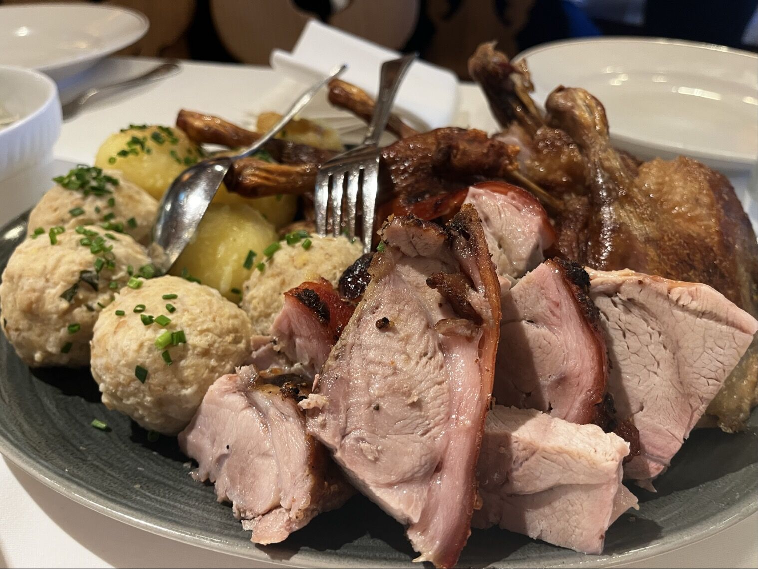 Auf einem großen Teller sind verschiedene Fleischgerichte angerichtet, darunter saftiges Schweinefleisch, knusprige Hähnchenteile, und große Klöße, umgeben von Kartoffeln. Die Speisen sind liebevoll angerichtet und verleihen einem festlichen Mahl einen reichhaltigen Eindruck.